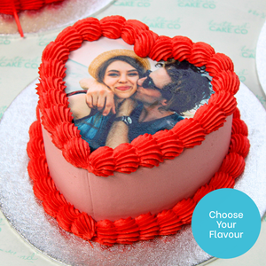 Heart-shaped cake with red icing and a photo of two people on top.